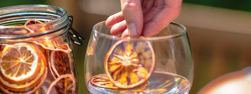 Fruitanicals - Practicality & Waste reduction - Open jar of slices with hand placing a slice into a glass of gin