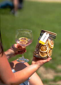 Outdoor shot of a gin and tonic with lemon slices, held alongside a jar of dehydrated lemon garnish.